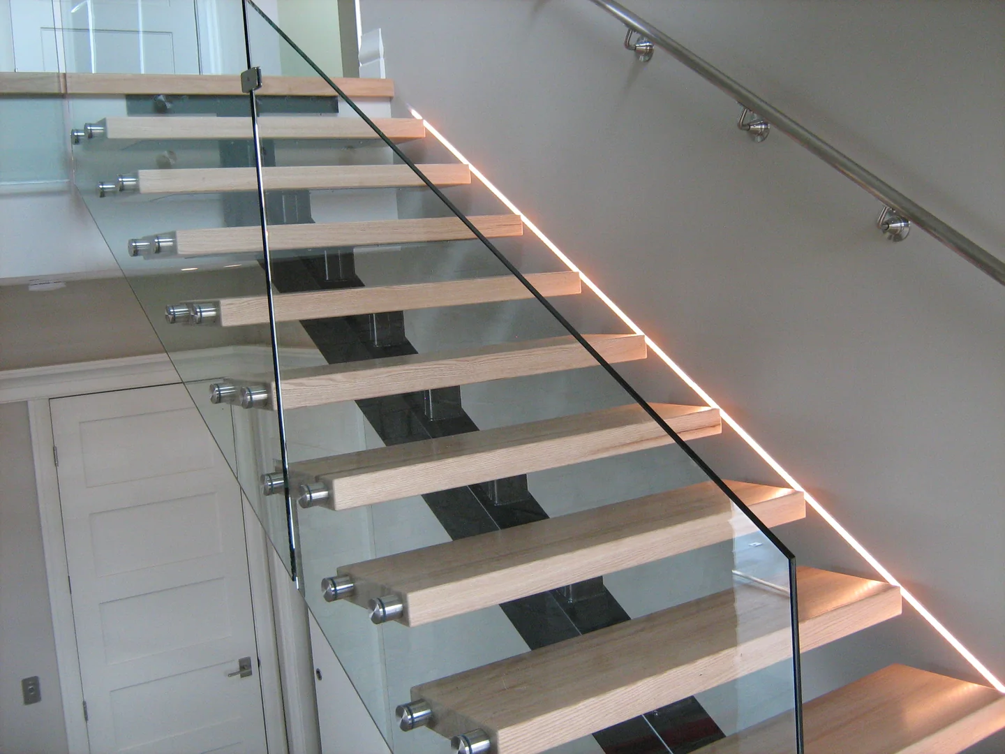 Glass-sided timber staircase with a warm light beside the treads